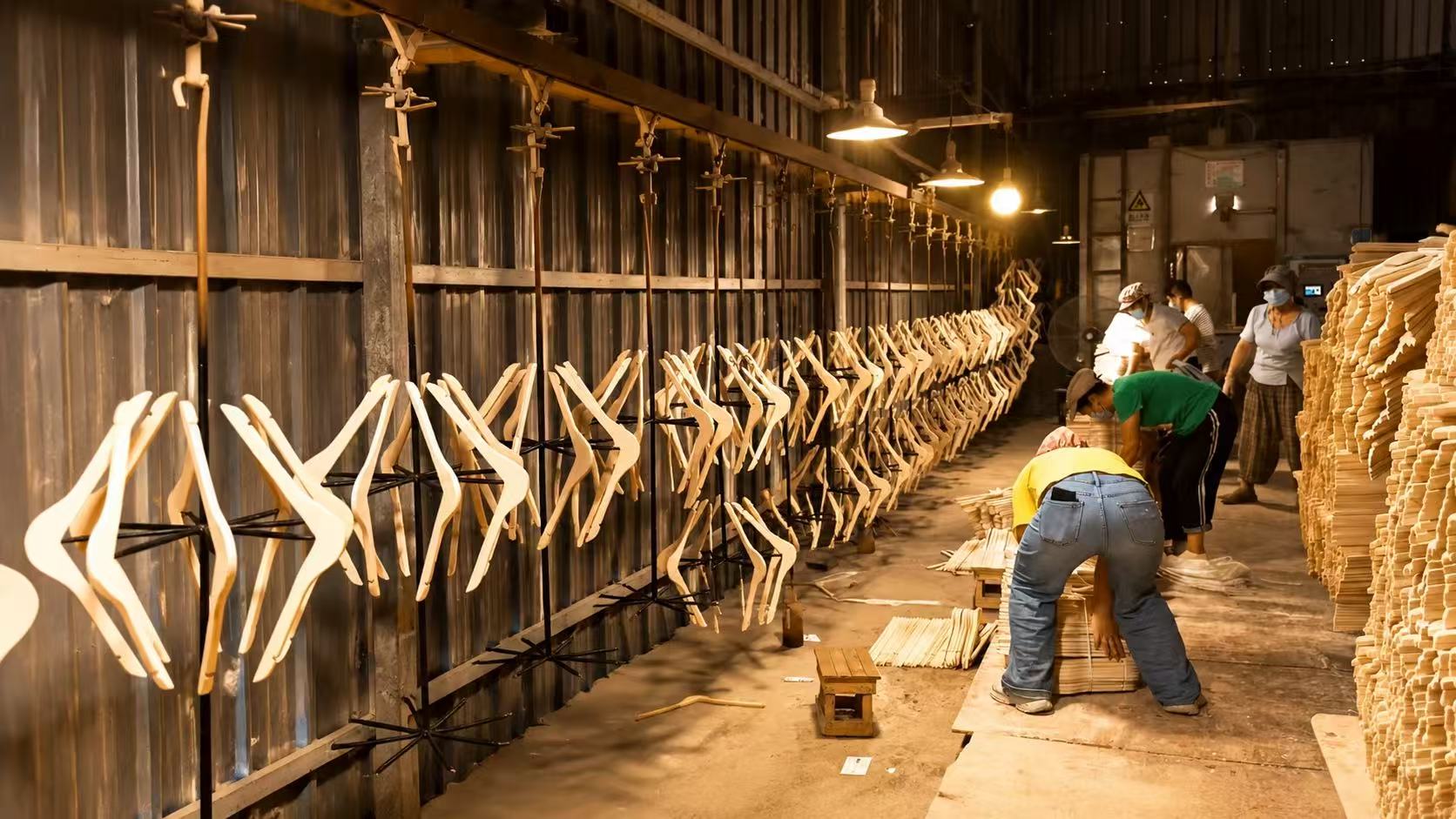 HANGIVA wooden hanger manufacturing line with workers and unfinished hangers.