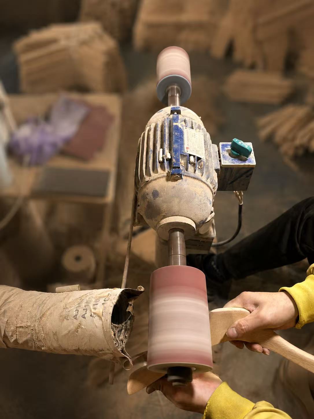 A worker holding a wooden hanger against a sanding drum.