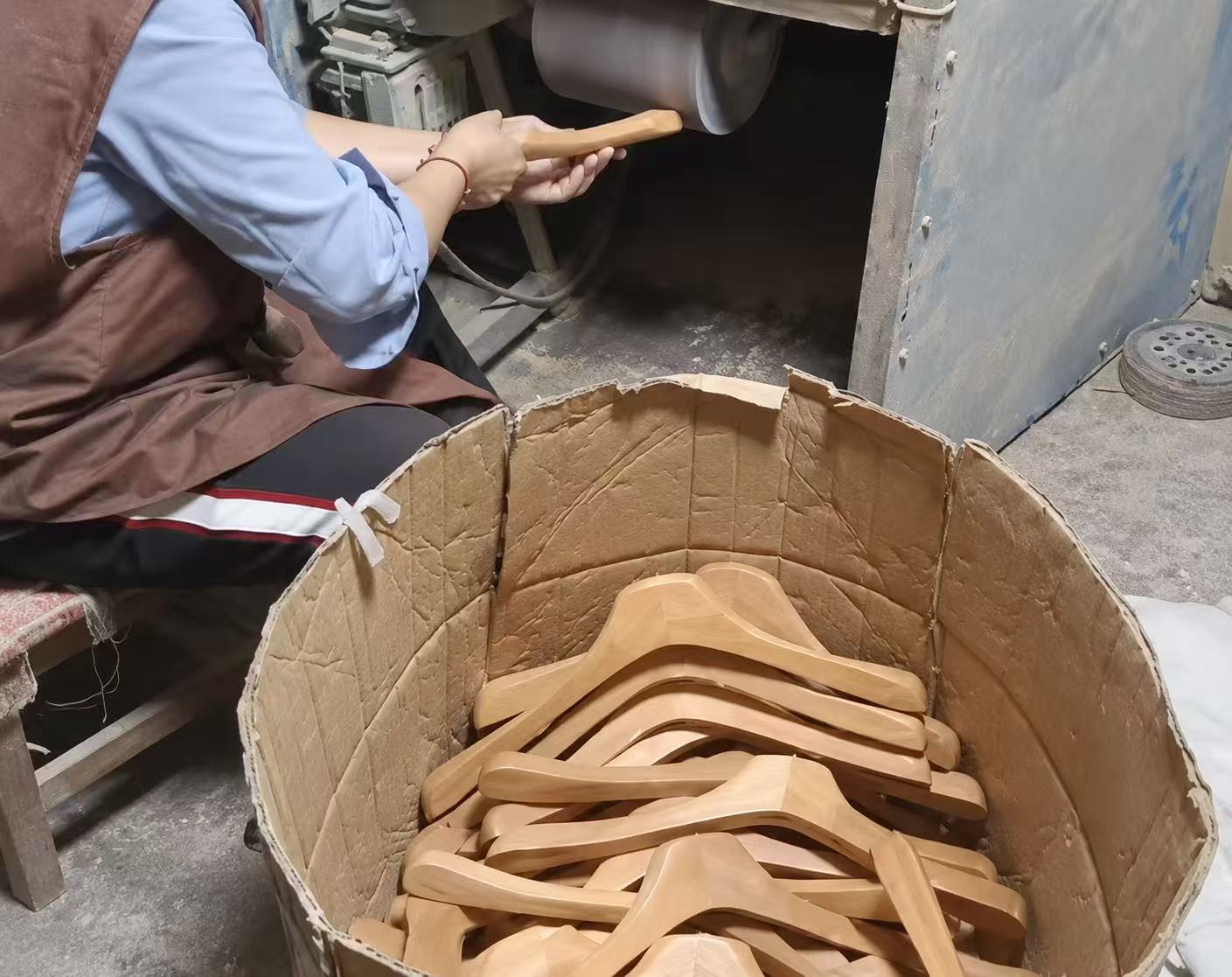 A worker refining a wooden hanger beside a container of hanger bodies.